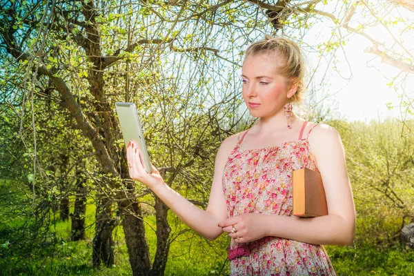 Woman in park outdoor with tablet and book deciding what to use — Stock Photo, Image