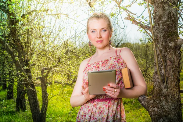 Woman in park outdoor with tablet and book deciding what to use — Stock Photo, Image