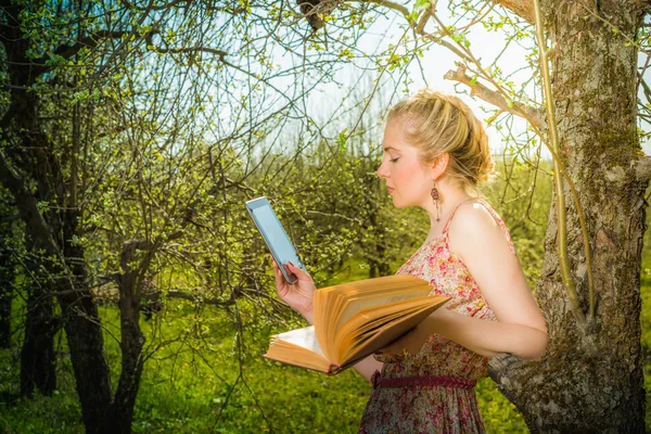 Woman in park outdoor with tablet and book deciding what to use — Stock Photo, Image