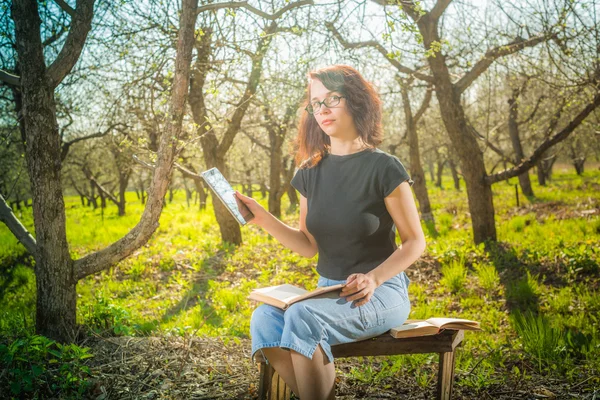 Woman in park outdoor with tablet and book deciding what to use — Stock Photo, Image