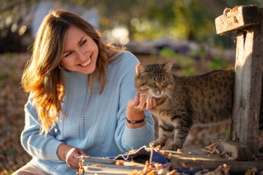 Açık mavi kazaklı gülümseyen genç bir kadının portresi güneşli bir sonbahar gününün tadını çıkarıyor. Altın yapraklar ve ılık güneş ışığı sonbahar mevsiminde yumuşak ve parlak bir atmosfer yaratır..