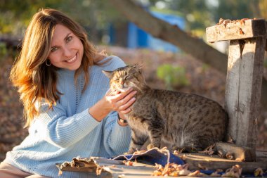 Açık mavi kazaklı gülümseyen genç bir kadının portresi güneşli bir sonbahar gününün tadını çıkarıyor. Altın yapraklar ve ılık güneş ışığı sonbahar mevsiminde yumuşak ve parlak bir atmosfer yaratır..