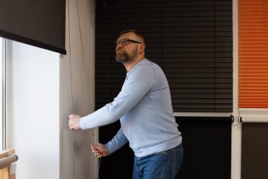 Küçük işletme sahibi perakende satış salonundaki pencere perdelerini ayarlıyor. Modern bir ofiste çeşitli jaluziler, ürün kalitesi ve işlevselliği gösteriyor..