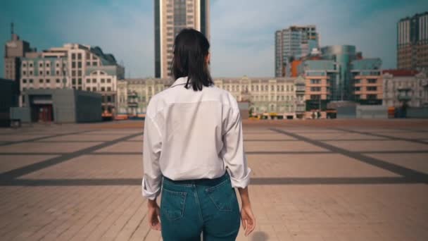 Πίσω όψη γυναίκα σε casual ρούχα περπάτημα στην πόλη στροφή προς την κάμερα — Αρχείο Βίντεο