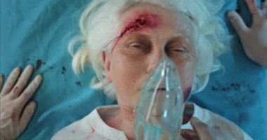 Sağlık görevlilerinin nabzını kontrol edip yaralı yaşlı bayan oksijen maskesini taktıkları yeri kapatın. Kliniğe giderken hastane sedyesinde yatan olgun bir kadın ölüyor. Kaza kavramı.