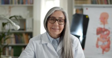 Kadın doktorun çevrimiçi danışmanlık yaparken el sallamasına ve gülümsemesine yakından bakın. Gözlüklü yaşlı bir kadın hastayla iletişim kurup kameraya bakıyor. Teletıp kavramı.