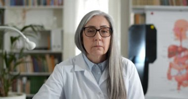 Hasta dinleyen ve kameraya bakarken başını sallayan yaşlı kadın doktoru yakından izleyin. Beyaz Rob 'daki kadın ofiste otururken görüntülü görüşme yapıyor. Teletıp kavramı.