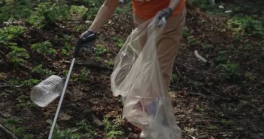 Çöp torbasında çöp toplarken çöp toplayıcı kullanan birinin kırpma görüntüsü. Çevre aktivisti ve gönüllü olarak parkı temizliyor. Ekoloji kavramı, temizlik ve doğa ile ilgilenmek..