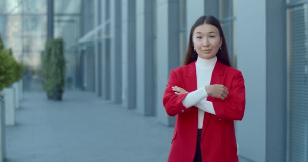 Portrait of cheerful asian businesswoman crossing arms while looking to camera. Crop view of successful woman ceo executive posing to camera while standing at street near office building. — Stock Video