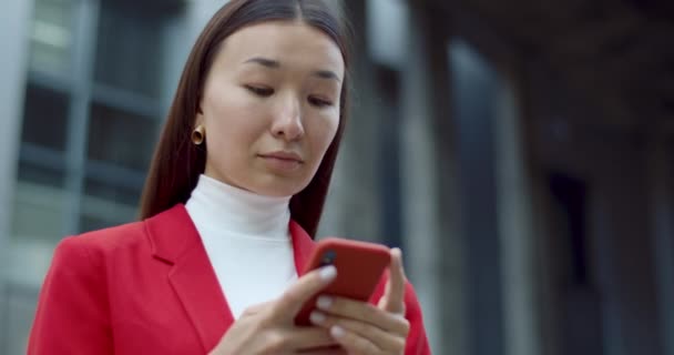 Вид знизу жінки, яка друкує повідомлення, використовуючи смартфон і стоячи на вулиці. Досить азіатська бізнес-леді торкається екрану телефону під час перегляду Інтернету. Концепція спілкування . — стокове відео
