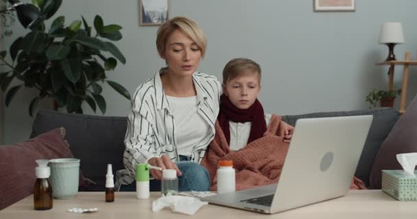 Bella mamma che parla e dà termometro al suo figlio adolescente mentre hanno una videochiamata. Famiglia guardando lo schermo del computer portatile pur avendo consultazione medica online con il medico. — Video Stock