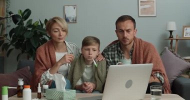 Genç bir aile evdeki kanepede otururken online tıbbi konsültasyon yapıyor. Anne, baba ve oğul doktorla iletişim kurarken dizüstü bilgisayara bakıyor. TeleHealth kavramı.