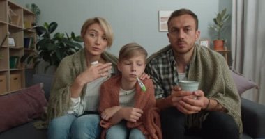 Genç anne doktorla görüntülü konuşma sırasında konuşuyor. Hasta bir aile kanepeye oturur ve internette tıbbi danışmanlık yaparken kameraya bakar. TeleHealth kavramı.