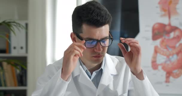 Crop view of young male doctor taking off glasses and massaging eyes. Homme en vol professionnel blanc regardant fatigué alors qu'il était assis à table dans un bureau médical. Concept de surmenage. — Video