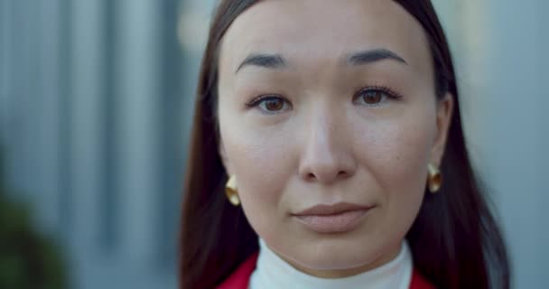 얼굴을 돌리며 카메라를 찾는 매력적 인 사업가의 모습을 가까이서 볼 수있다. 거리에 서 있는 동안 황금 귀걸이를 하고 있는 아시아 여성의 초상화. 헤드샷의 개념. — 비디오