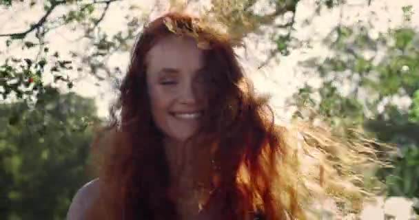 Portret van vrolijke jonge vrouw op zoek naar camera en glimlachen terwijl de wind waait haar haar.Crop view of millennial vrouwelijke persoon poseren in het park. Concept van positieve emoties. — Stockvideo