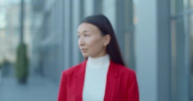 Çekici Asyalı bir kadının başını çevirip kameraya bakması. Şehir caddesinde dururken poz veren başarılı bir iş kadınının portresi. Yakınlaştır. Bulanık arkaplan.