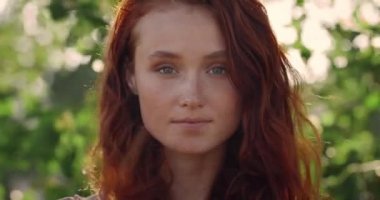 Kameraya bakan uzun kızıl saçlı güzel bir kadın modelin vesikalığı. Genç ve neşeli bir kadının poz verişine yakından bakın. Yaşam tarzı kavramı. Bulanık yeşil arkaplan.