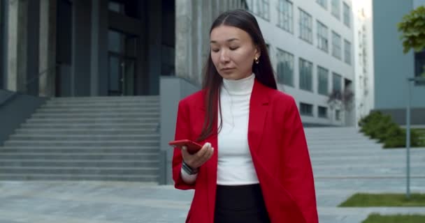 Recortar vista de buen aspecto mujer de negocios asiática responder a la llamada telefónica y hablar. Señora exitosa con cara seria conversando y caminando por la calle en el área de negocios. — Vídeo de stock