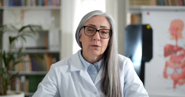 Schnittansicht einer Frau in einer Brille, die dem Patienten ein Röntgenbild während eines Videogesprächs zeigt. Ärztinnen in weißen Roben reden und schauen in Arztpraxis in die Kamera. — Stockvideo
