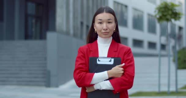 書類のフォルダを保持し、カメラを探して深刻なアジアの女性のオフィスワーカーの肖像画。成功した女性のCEOポーズのミステリービューでカメラに立ちながら. — ストック動画