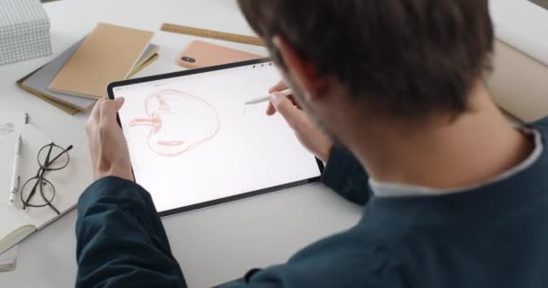 Vista por encima del hombro del diseñador gráfico masculino creando ilustración en la tableta.Talanted ilustrador utilizando almohadilla digital y lápiz mientras está sentado en el lugar de trabajo y haciendo boceto . — Vídeos de Stock