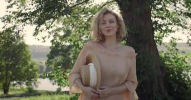 Parkta yürürken gülümseyen şapkalı hoş bir kadın. Kısa sarı dalgalı saçlı ve kameraya bakan güzel kadın modelin portresi. Kadın portresi ve yaşam tarzı kavramı. Gün ışığı.