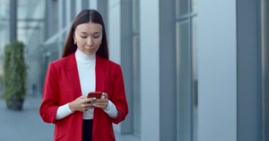 Sosyal medyada iletişim kuran ve gülümseyen neşeli kadın görüntüsü. Akıllı telefon kullanan ve sokakta yürürken telefon ekranına bakan güzel bir kadın CEO yöneticisi..