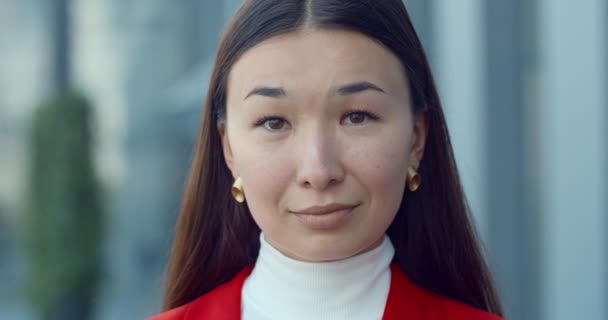 매력적 인 사업가가 카메라 앞을 보고 포즈를 취하는 것을 클로즈업 합니다. 사업 지역의 도시 거리에 황금 귀걸이를 하고 있는 예쁜 동양 여성의 초상화. 헤드샷의 개념. — 비디오