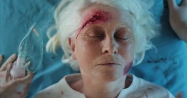 Doktorların elleri yaralı bir kadın takarken gördüğü en iyi görüntü oksijen solunum maskesi. Bilinci yerinde olmayan, kafa travması geçiren yaşlı bir kadın hastaneye giderken tıbbi nakil sedyesinde yatıyor..