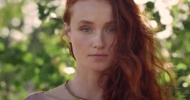 Kameraya bakan, uzun kızıl saçlı, güzel bir kadının yakın görüntüsü. Çekici bir kadının poz verdiği portre. İnsanların vesikalık fotoğrafı. Bulanık yeşil arkaplan.