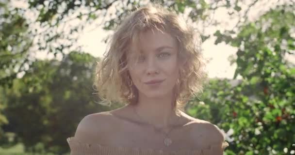 Ritratto di attraente donna con capelli biondi corti che guarda alla macchina fotografica alla luce del giorno. Vista Crop di giovane donna in posa mentre in piedi nel parco. Zoom in avanti. Concetto di lifestyle. — Video Stock