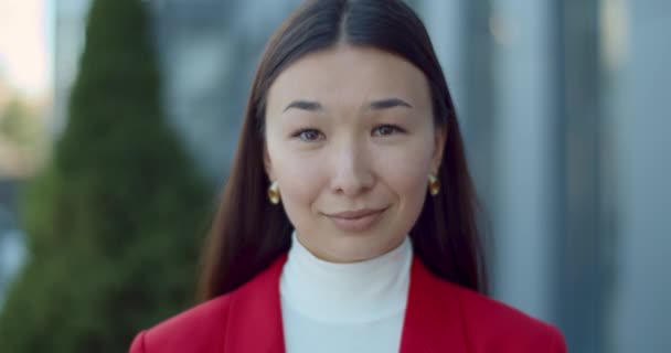 Közelről láthatjuk az örömteli nőt, aki a kamerába néz és pózol. Egy vonzó ázsiai üzletasszony portréja, aki mosolyog, miközben a város utcájában áll. Fogalom az emberek fejlövés. — Stock videók