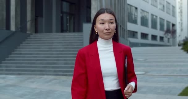 Vista de la cosecha de la ocupada mujer de negocios que lleva la carpeta de documentos de papel y mirando la pantalla del reloj inteligente. Mujer de buen aspecto con éxito en ropa elegante caminando en la calle en la zona de negocios. — Vídeo de stock