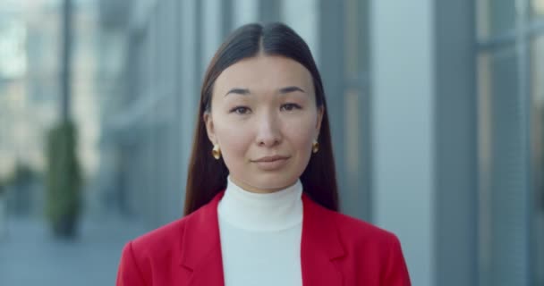 Retrato de mujer de negocios asiática en pendientes dorados mirando y posando a cámara. Primer plano de la exitosa dama de pie en la calle de la ciudad en el área de negocios. Concepto de personas en la cabeza. — Vídeo de stock