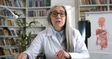 Kadın doktorun kameraya bakarken el sallaması ve hastayla iletişim kurması. Rob 'da bir kadın ofiste otururken görüntülü konuşma ve yazma yapıyor. Teletıp kavramı.