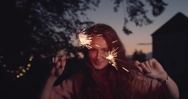 Crop view of millennial woman with long hair posing while looking to camera and smiling. Portrait de mannequin féminine ludique dansant et étincelant en se tenant debout dans le parc du soir. — Video