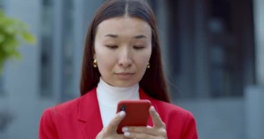 İyi haberler verirken ve gülümserken neşeli bir kadının yazı yazışına yakından bakın. Çekici Asyalı iş kadını akıllı telefon kullanıyor ve sokakta dikilirken telefon ekranına bakıyor..