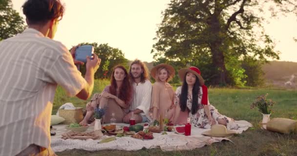 Hombre tomando fotos con cámara instantánea de personas positivas diversas en el parque. Jóvenes amigos sonriendo y posando mientras hacen picnic y se sientan en la hierba. Concepto de momentos felices. — Vídeos de Stock
