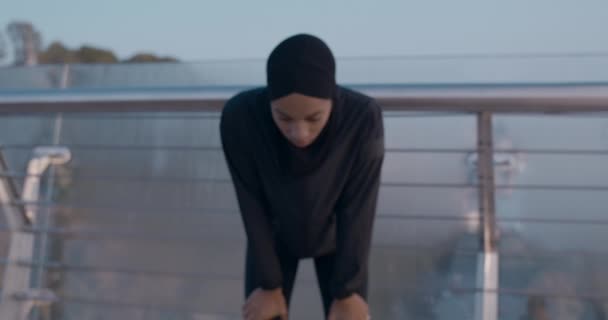 Молода мусульманка в хіджабі намагається зловити подих після бігу, стоячи на вулиці. Жіноча емоційна людина нахиляється і кричить, дивлячись на камеру. Збільшити масштаб . — стокове відео