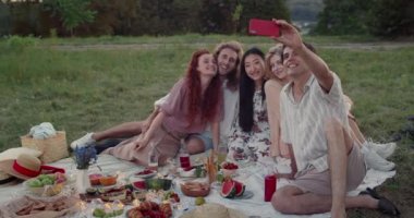 Gençler çimlerin üzerinde otururken ve piknik yaparken akıllı telefon ön kamerası kullanıyorlar. Çeşitli bin yıllık arkadaşlar selfie çekiyorlar ve fotoğrafa bakıyorlar. Arkadaşlık kavramı ve olumlu.