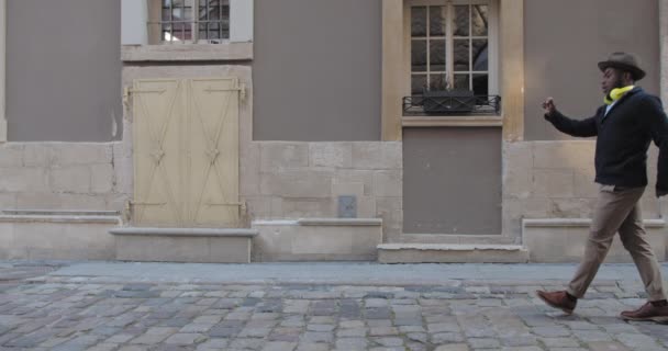 Bel homme afro-américain en chapeau dansant tout en marchant le long de la vieille rue de la ville. Barbu gars heureux portant des vêtements à la mode chantant et se déplaçant dans la rime. Concept d'émotions. — Video