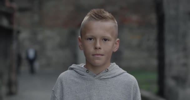 Portret van een tiener met een capuchon die naar de camera kijkt. Close-up uitzicht op schattige jongen poseren in de oude stad straat. Concept van kinderen en levensstijl. — Stockvideo