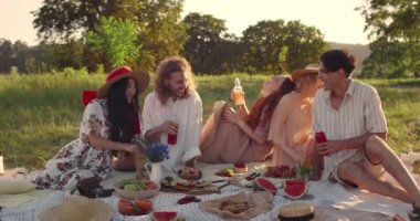 Milenyum arkadaşları parkta çimenlerde otururken gülüyorlar. Piknik yaparken cam şişe tutan neşeli kadın ve erkekler. Olumlu duygular kavramı.