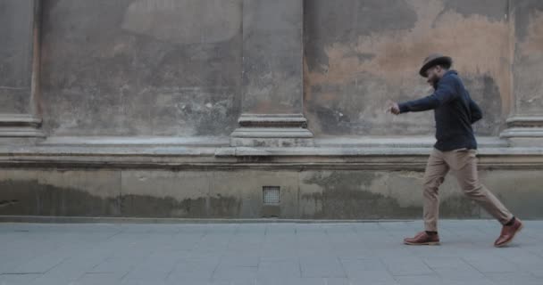 Guapo afroamericano hombre bailando mientras camina a lo largo de la vieja calle de la ciudad. Hombre barbudo sonriente vistiendo ropa elegante y moviéndose en rima. Concepto de emociones. Al aire libre. — Vídeos de Stock