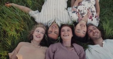 Tepeden tırnağa çimenlerin üzerinde yatan ve gülümseyen neşeli arkadaşların en iyi görüntüsü. Bir grup genç insan birlikte eğleniyor. Olumlu anlar ve arkadaşlık kavramı.