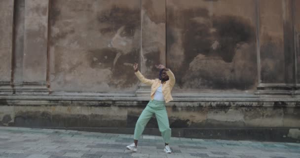 Emocional mujer afroamericana bailando y haciendo muecas en la vieja calle de la ciudad. Loco millennial mujer persona mirando a la cámara mientras hace movimientos divertidos. Concepto de buen humor. — Vídeos de Stock