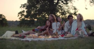 Bir grup neşeli insan çimlerin üzerinde oturup piknik yaparken iletişim kuruyor. Güzel bir kadın akşam arkadaşlarıyla güzel vakit geçirirken gitar çalıyor..