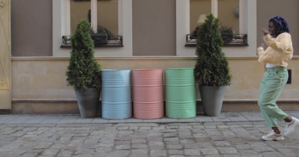 Persona femminile che sorride e balla mentre cammina per la strada della città. Afro-americana donna allegra che si trasferisce in rhytm all'aperto. Concetto di buon umore. Canne colorate sullo sfondo. — Video Stock