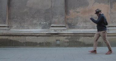 Eski şehir caddesinde yürürken dans eden yakışıklı milenyum erkeği. Şapkalı, sakallı, şık bir adam. Kafiyeli hareket ederken mutlu görünüyor. Duygu kavramı. Açık havada..